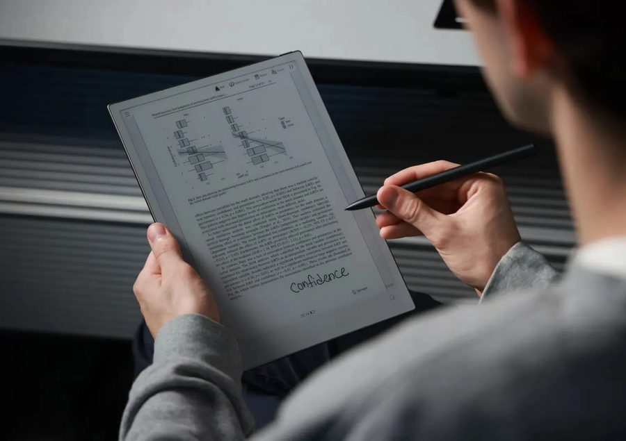 Hands holding an iFLYTEK AINOTE 2 e-paper notebook and writing on it with its stylus